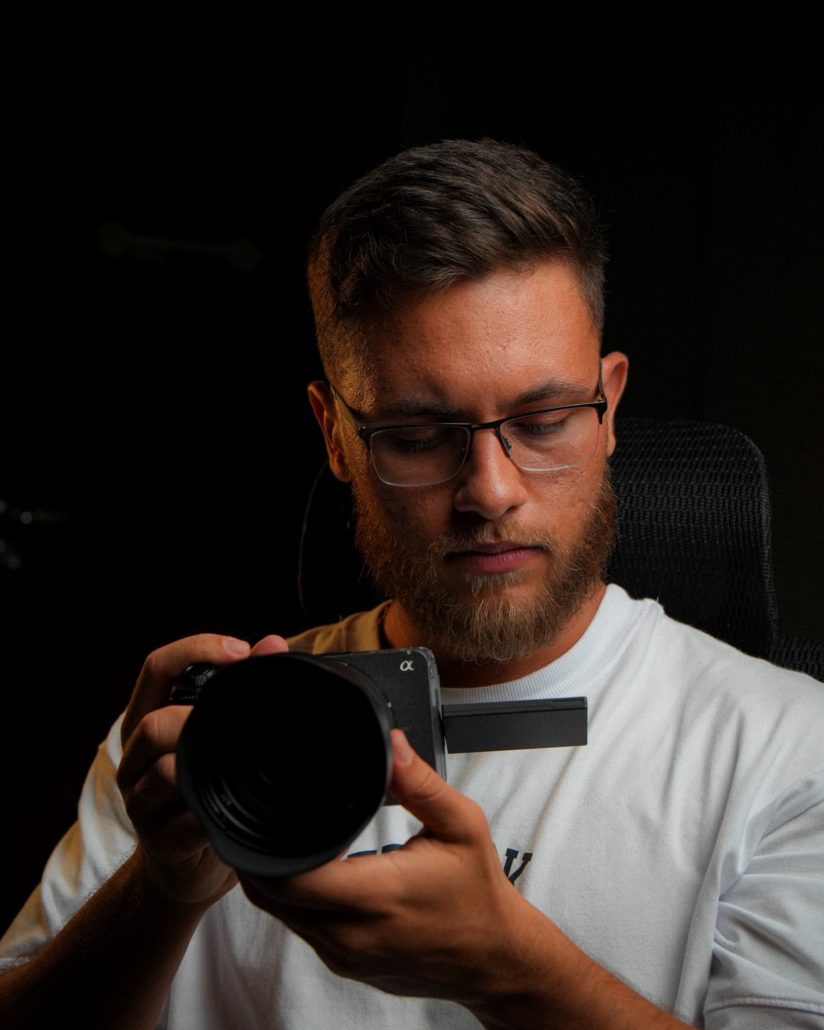 Matheus Castro segurando uma câmera Sony, iluminado por luz lateral sobre fundo escuro